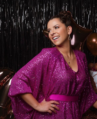 Aniversariante de vestido rosa com paetês rindo em frente a balões